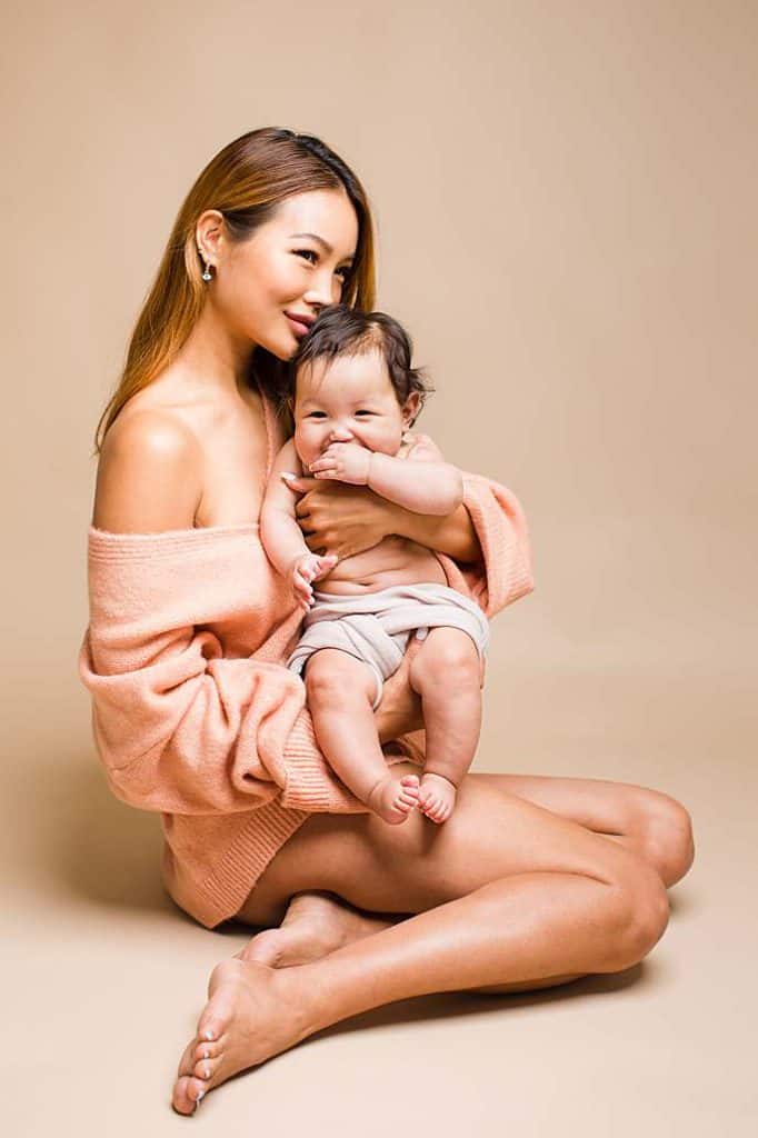 Natural studio photoshoot of mother cuddling baby daughter, both dressed in soft tones, captured in London for a warm and intimate family portrait. Baby is giggling cutely.