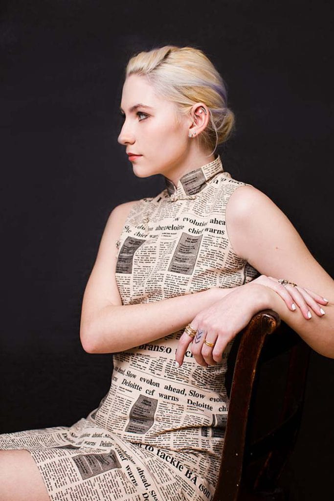platinum-blonde-hair-girl-sitting-in-chair-dressed-in-newspaper-unusal-bold-print-chines-dress