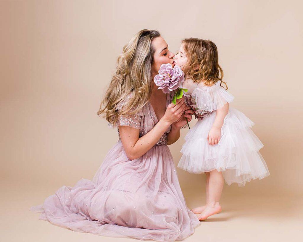 Young daughter kisses her smiling mother in matching white outfits, captured in an intimate family portrait session.