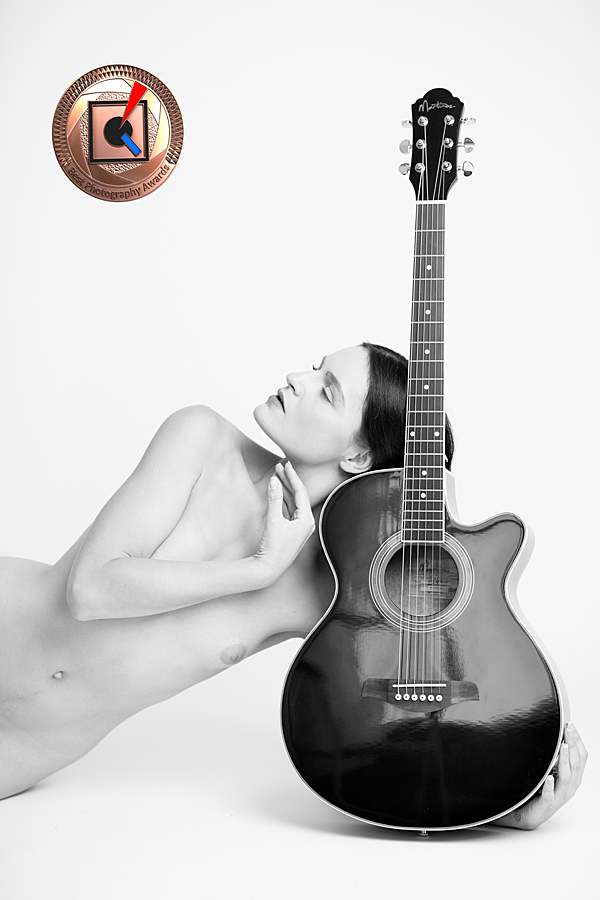 Award-winning nude boudoir portrait featuring a woman posing with a guitar, elegant fine art nude photography London by female photographer Belinda Burton.