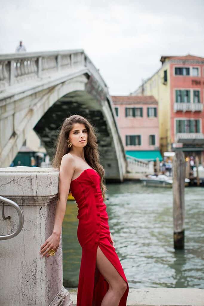 girl-in-red-dress-leaning-on-venice-footbridge-in-front-of-canal-coloured-houses