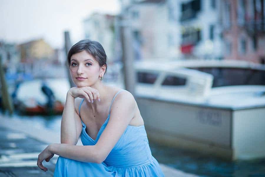 venice-photo-shoot-girl-blue-dress-in-front-of-canal-waterway-hand-under-chin-looking-dreamy
