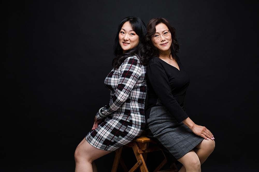 mother-daughter-photo-shoot-grown-up-daughter-leaning-against-mother-black-background