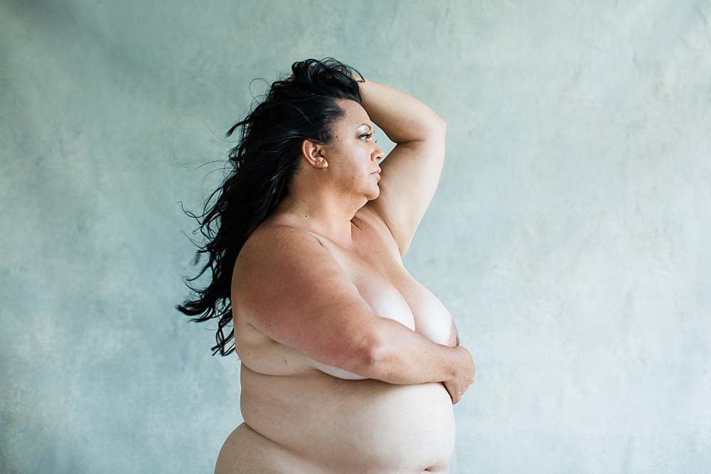 plus-size-boudoir-photography-fine-art-nude-woman-with-stomach-and-rolls-in-front-of-blue-background