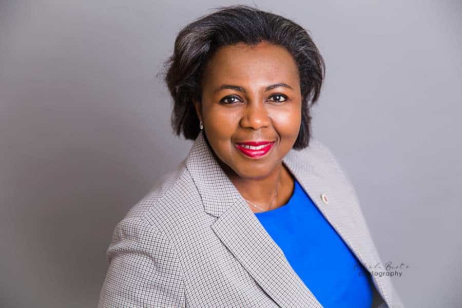 business-portrait-nigerian-woman-in-grey-suit-smiling-into-camera-grey-background-london