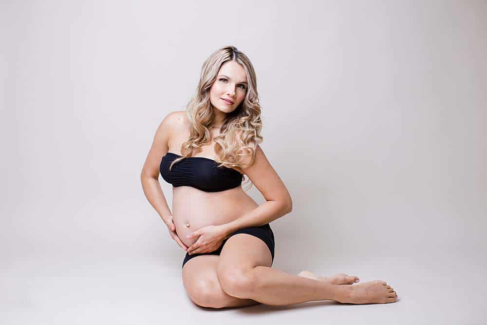 prepnancy-photography-london-pregnant-photo-of-woman-sitting-on-floor-in-black-shorts-and-bra-top-embracing-belly