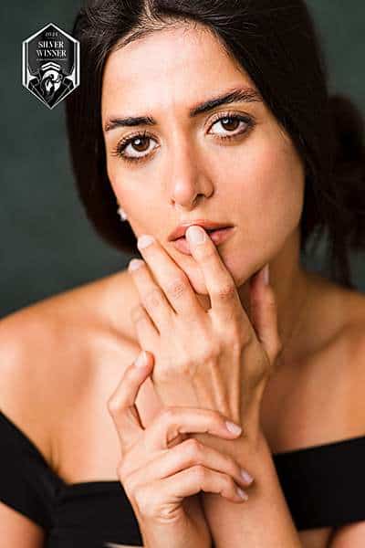 Close-up studio portrait of a woman in a black off-shoulder dress posing with hands near her face, Silver Winner in London studios photography.