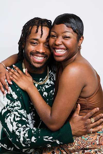 Smiling man and woman of colour embracing each other joyfully during a couple studio photography session, radiating warmth and connection.