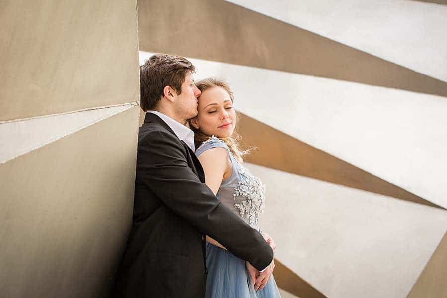 Couple in elegant attire embracing in front of a modern architectural wall in the City of London