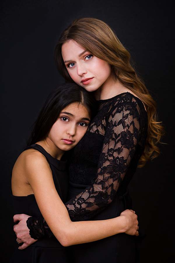 Elegant mother and daughter portrait in a London studio with both mother and daughter in black dresses in front of black background, capturing a close family bond in professional photography session.